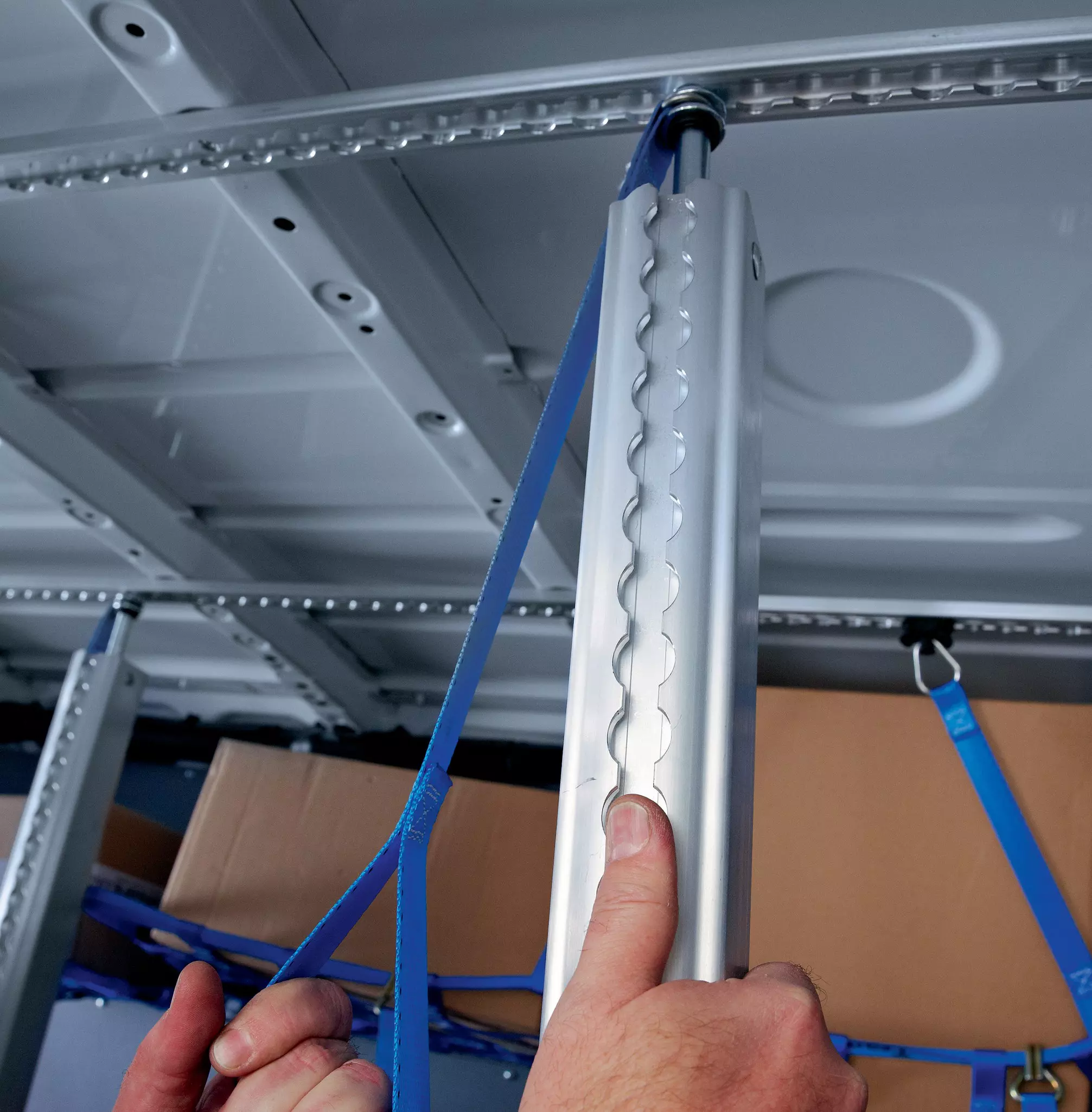 Hände montieren eine vertikale Aluminium-Sperrstange zwischen Decken- und Bodenschiene im Transporter