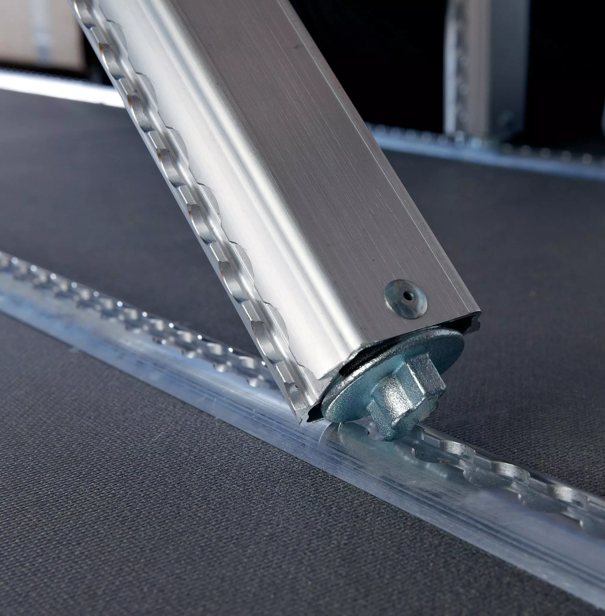 Unteres Ende einer Aluminium-Sperrstange mit Drehfuß in einer gelochten Bodenschiene