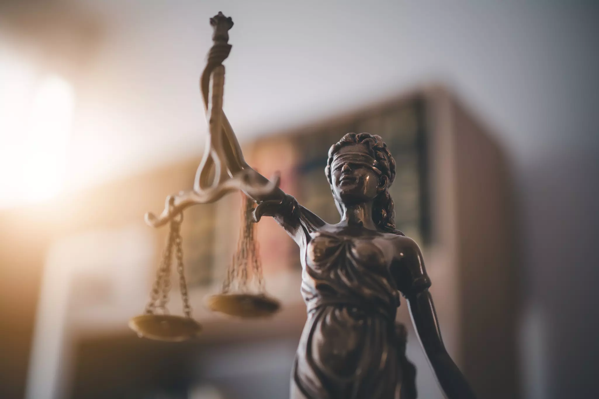 Bronzene Justitia-Statue mit Waage und Augenbinde vor unscharfem Bücherregal