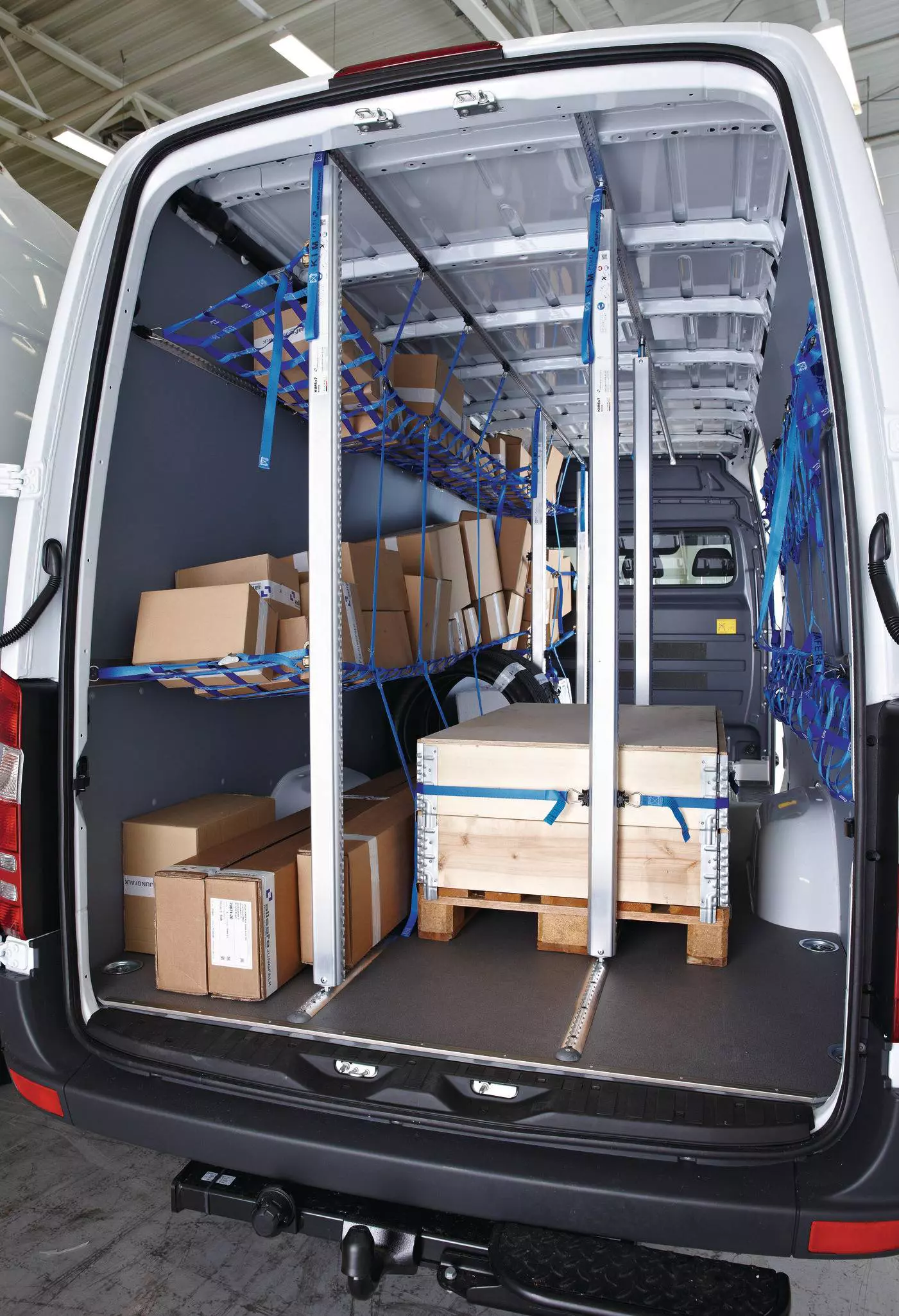 Transporter-Laderaum mit vertikalen Sperrstangen und blauen Netzen zur mehrstufigen Ladungssicherung